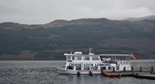 The 'Cruise Loch Lomond' boat moving along the water, with mountains behind it