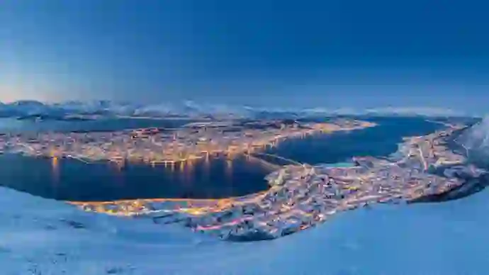 View of Tromso in the snow, at night time with light from the buildings lighting up the town