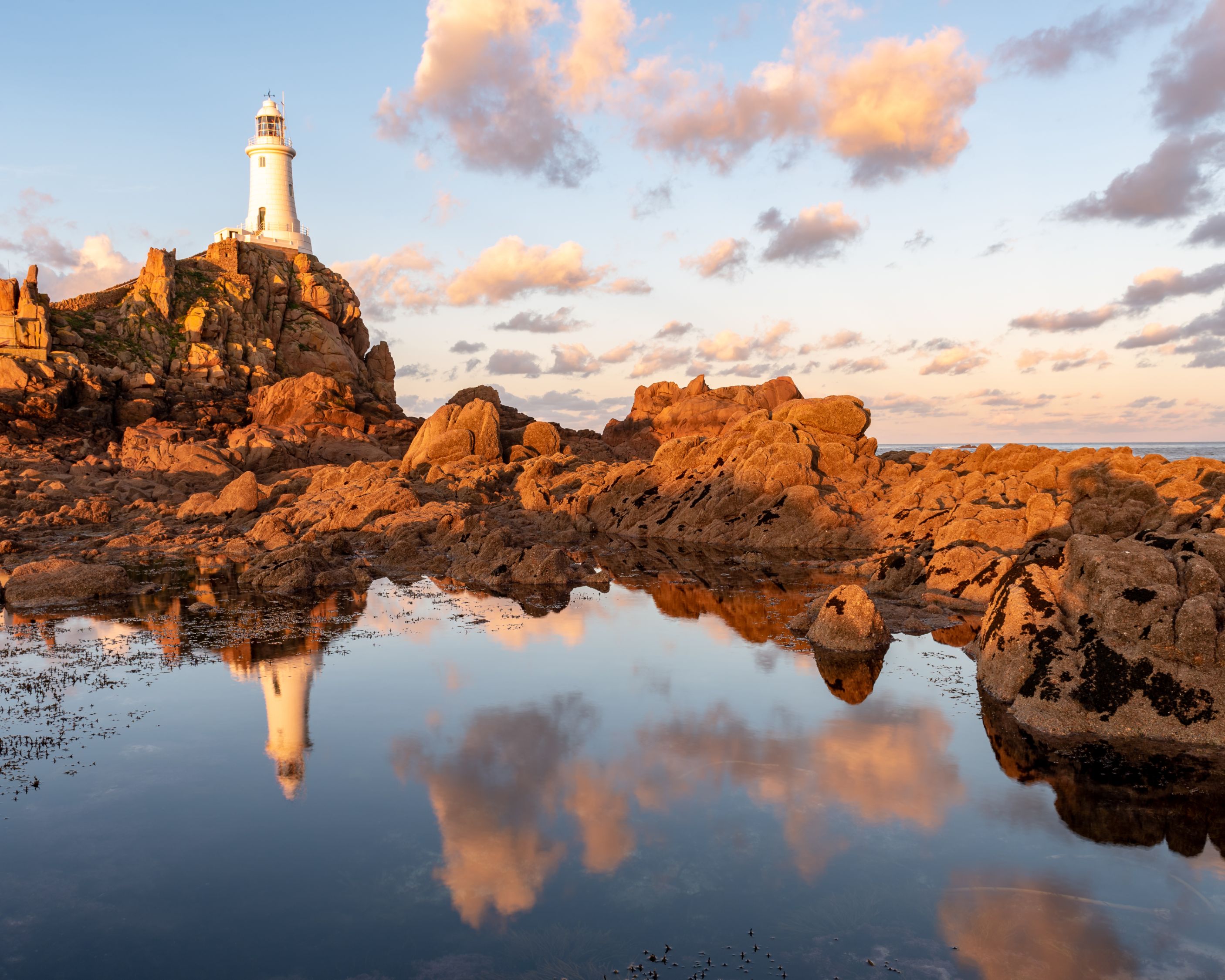 Low angle shot of La Corbiere Lighthouse, showing a small body of water below it the group of rocks around it