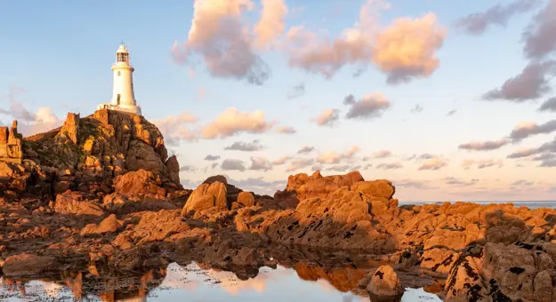Low angle shot of La Corbiere Lighthouse, showing a small body of water below it the group of rocks around it