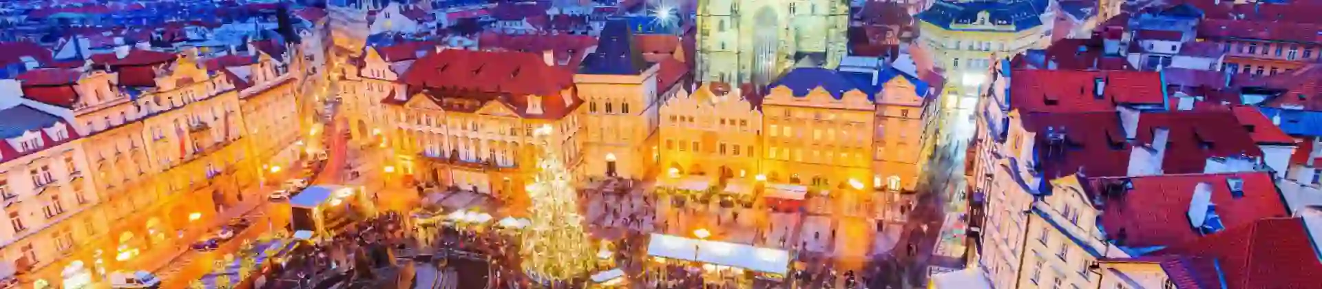 High angle shot of a Christmas market in the town square of Prague, showing a lit up gothic church with two towers and a large lit up Christmas tree