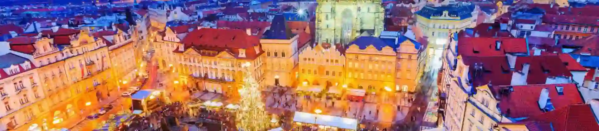 High angle shot of a Christmas market in the town square of Prague, showing a lit up gothic church with two towers and a large lit up Christmas tree