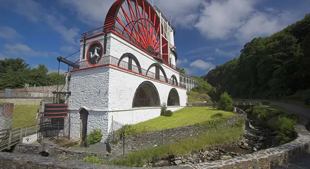 Shot of the red and white Laxey Water Wheel, showing the Isle of Man flag on the side and the grass and stone walls below it