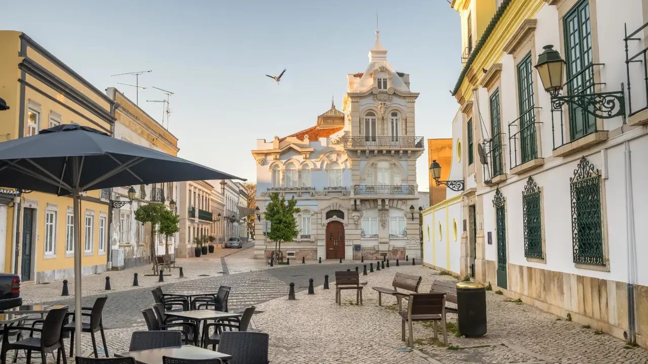 City centre of Faro, Algarve, showing cobbled streets, café tables and benches along the pavement, and Belmarco Palace at the end of the street