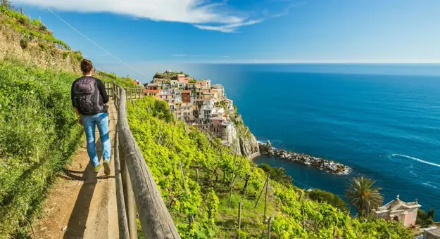 A person walking along a cliffside path in Cinque Terre, overlooking colourful buildings and the blue sea