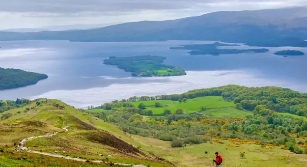 High angle view of Loch Lomond and Trossachs National Park, with a man wearing a red jacket walking down the mountain