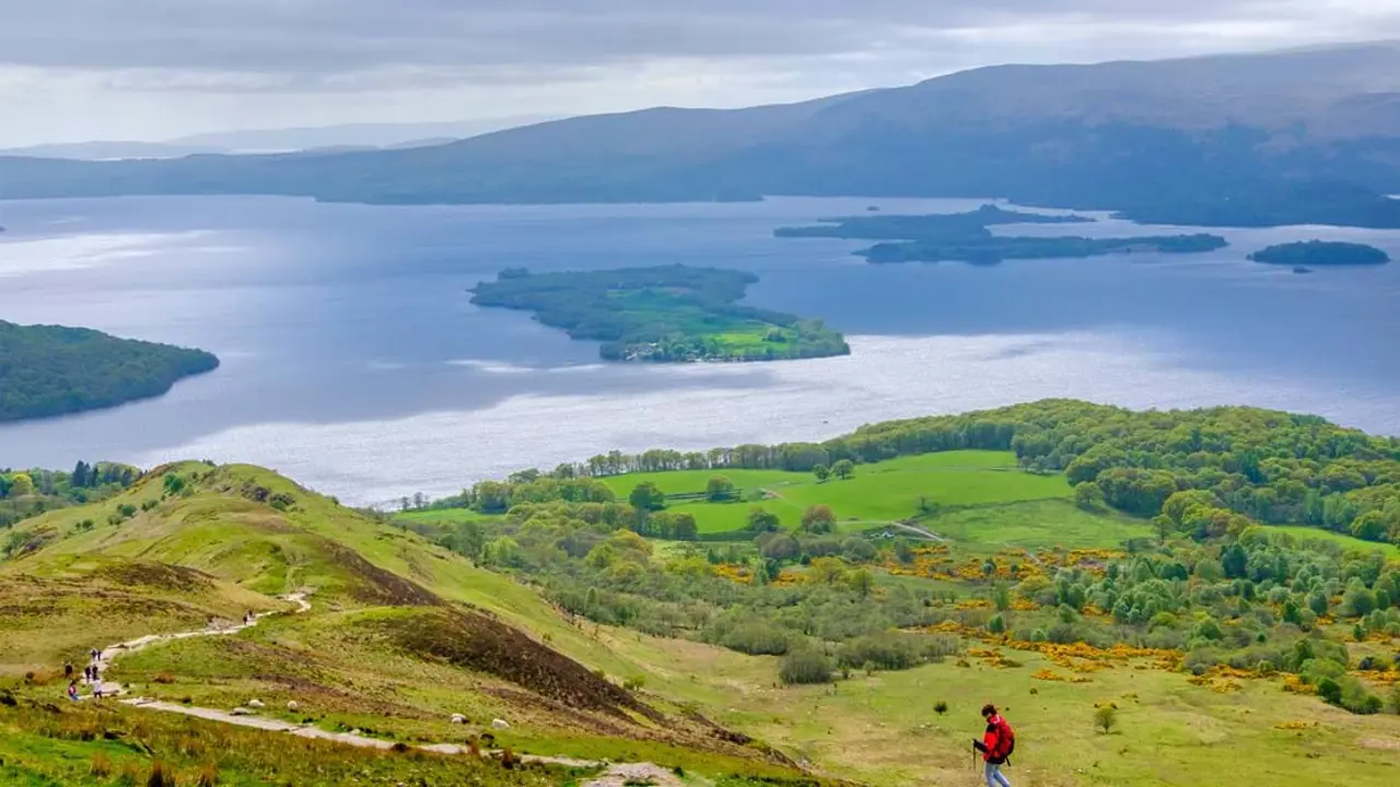 High angle view of Loch Lomond and Trossachs National Park, with a man wearing a red jacket walking down the mountain