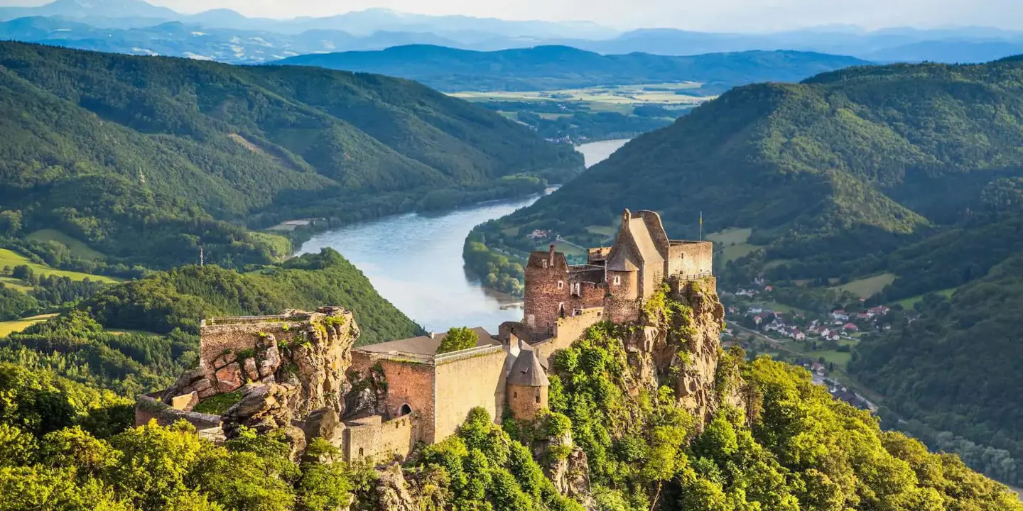 Ruins of a medieval castle perched on a rocky hilltop overlooking the Danube River in the Wachau Valley, Austria, surrounded by lush green hills and distant mountains