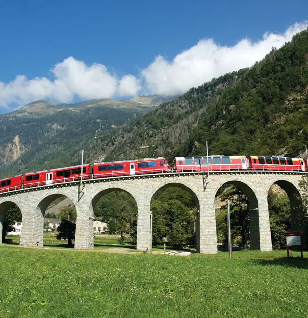 The Bernina Express going across a bridge, with grassy mountains in the background