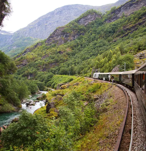 Train going through the mountains by a small stream of water