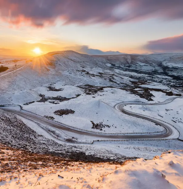 View of the Peak District at winter, with snowy mountains and the sun creeping over the edge of the land