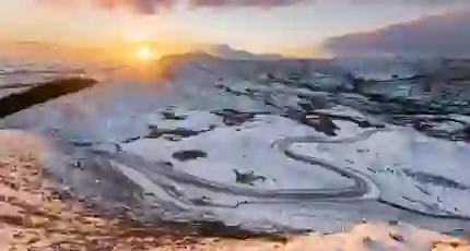 View of the Peak District at winter, with snowy mountains and the sun creeping over the edge of the land