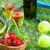 Close up of two glasses of champagne, a basket of strawberries, tennis balls and rackets on some grass