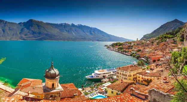 Scenic view of Limone sul Garda, a picturesque lakeside town on Lake Garda, Italy, with colourful buildings nestled against steep mountain cliffs and the calm blue lake in the foreground