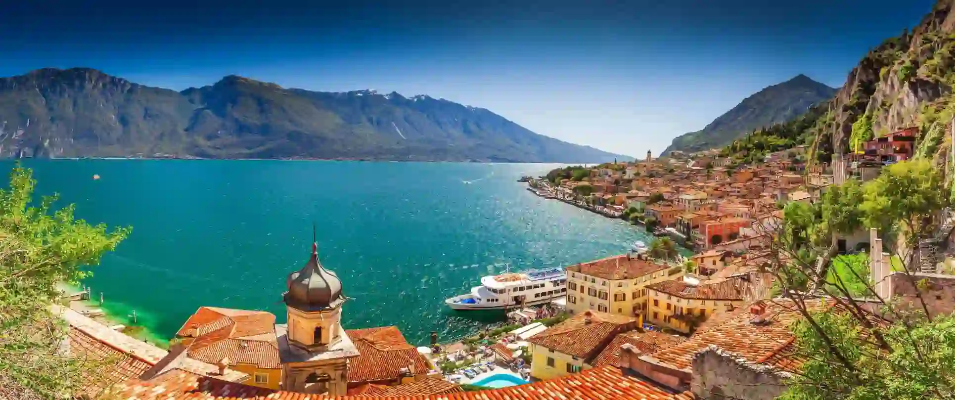 Scenic view of Limone sul Garda, a picturesque lakeside town on Lake Garda, Italy, with colourful buildings nestled against steep mountain cliffs and the calm blue lake in the foreground