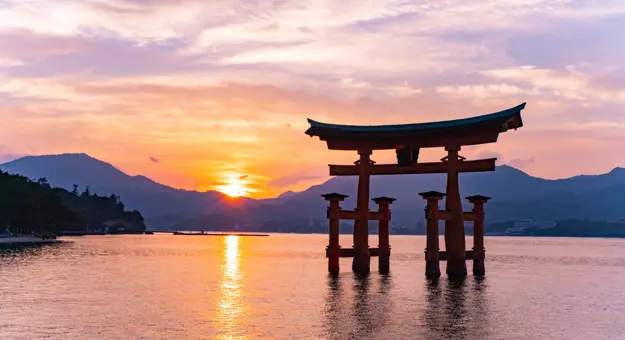 Panoramic view of the beautiful and monumental Floating bridge called Torii of Itsukushima Shrine with a beautiful orange sunset in the background