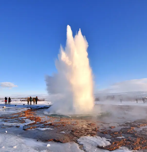 Erupting geysur, surrounded by rocks and ice. People stood watching