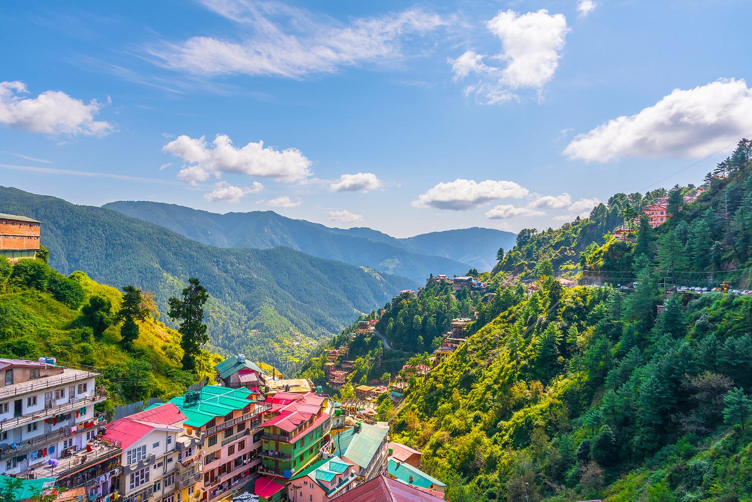A panoramic view of Shimla’s colourful hillside buildings surrounded by lush green mountains and misty clouds in the Himalayan foothills