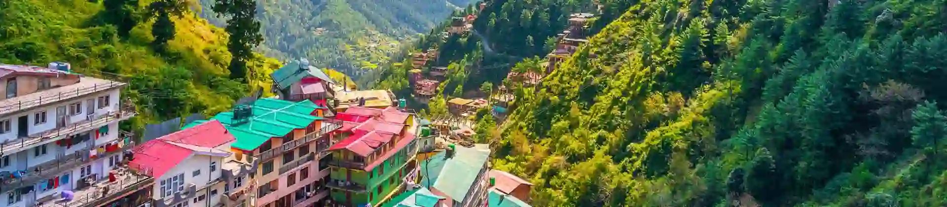 A panoramic view of Shimla’s colourful hillside buildings surrounded by lush green mountains and misty clouds in the Himalayan foothills