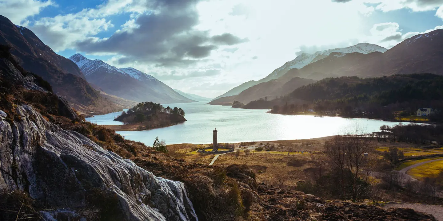 Zoomed out image of Glenfinnan Monument Scotland amongst the highlands with a view of Lock Shiel