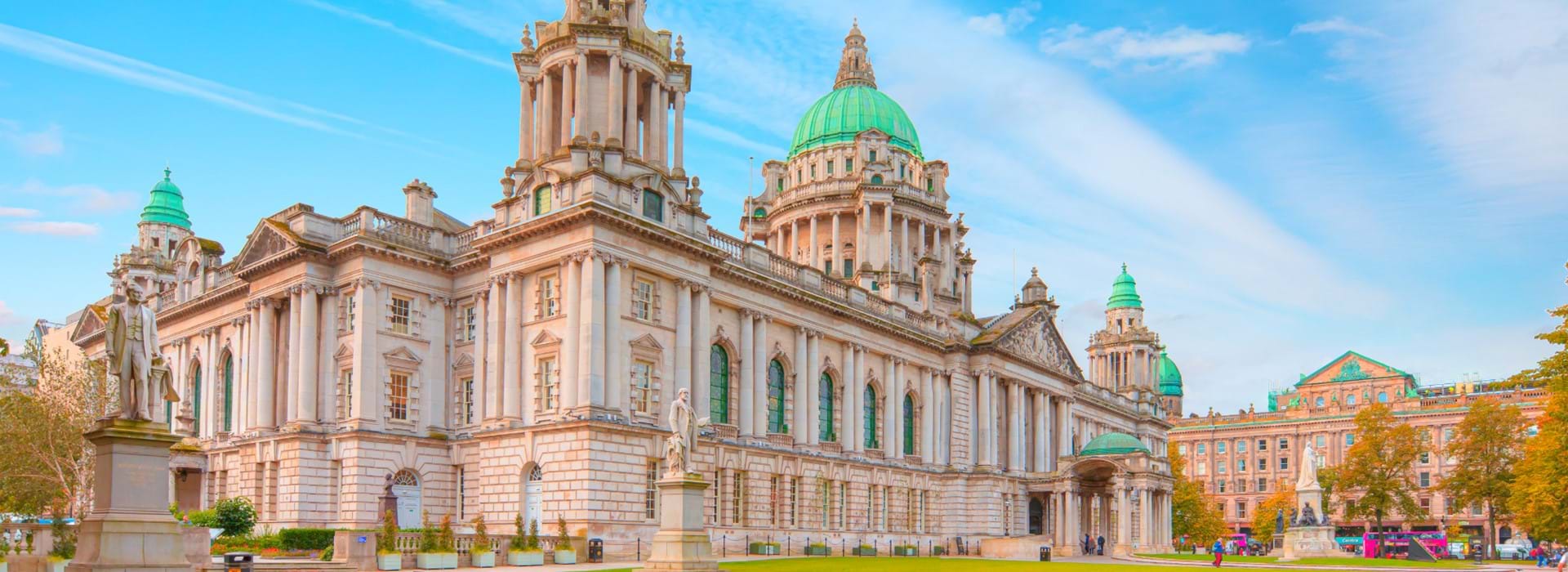 Shot of the Belfast town hall, showing the statues stood outside it and its' bright green turrets, with a blue sky behind it