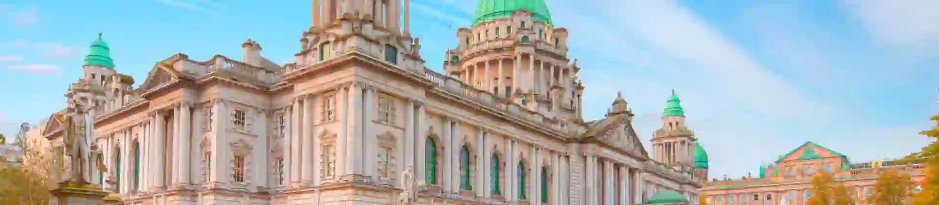 Shot of the Belfast town hall, showing the statues stood outside it and its' bright green turrets, with a blue sky behind it