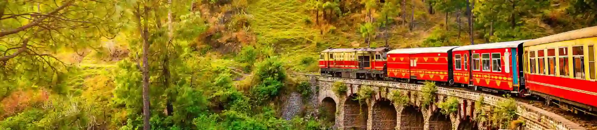 The heritage toy train crossing a railway bridge on the Kalka–Shimla route, surrounded by lush green hills and trees