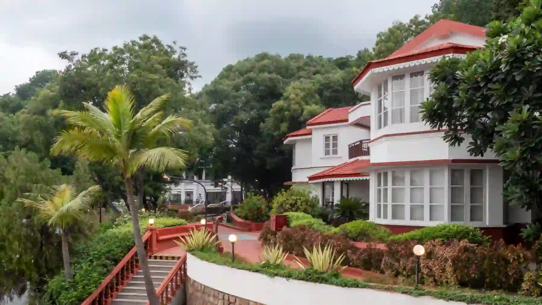 Two-storey exterior of The Taj Gateway Hotel in Madurai, featuring classic red and white paintwork, surrounded by trees, with an external staircase leading up to the building
