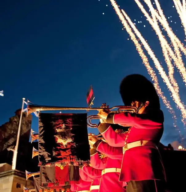 The Royal Edinburgh Military soldiers playing fanfare on trombones, suspended with flags in front of Edinburgh castle and fireworks