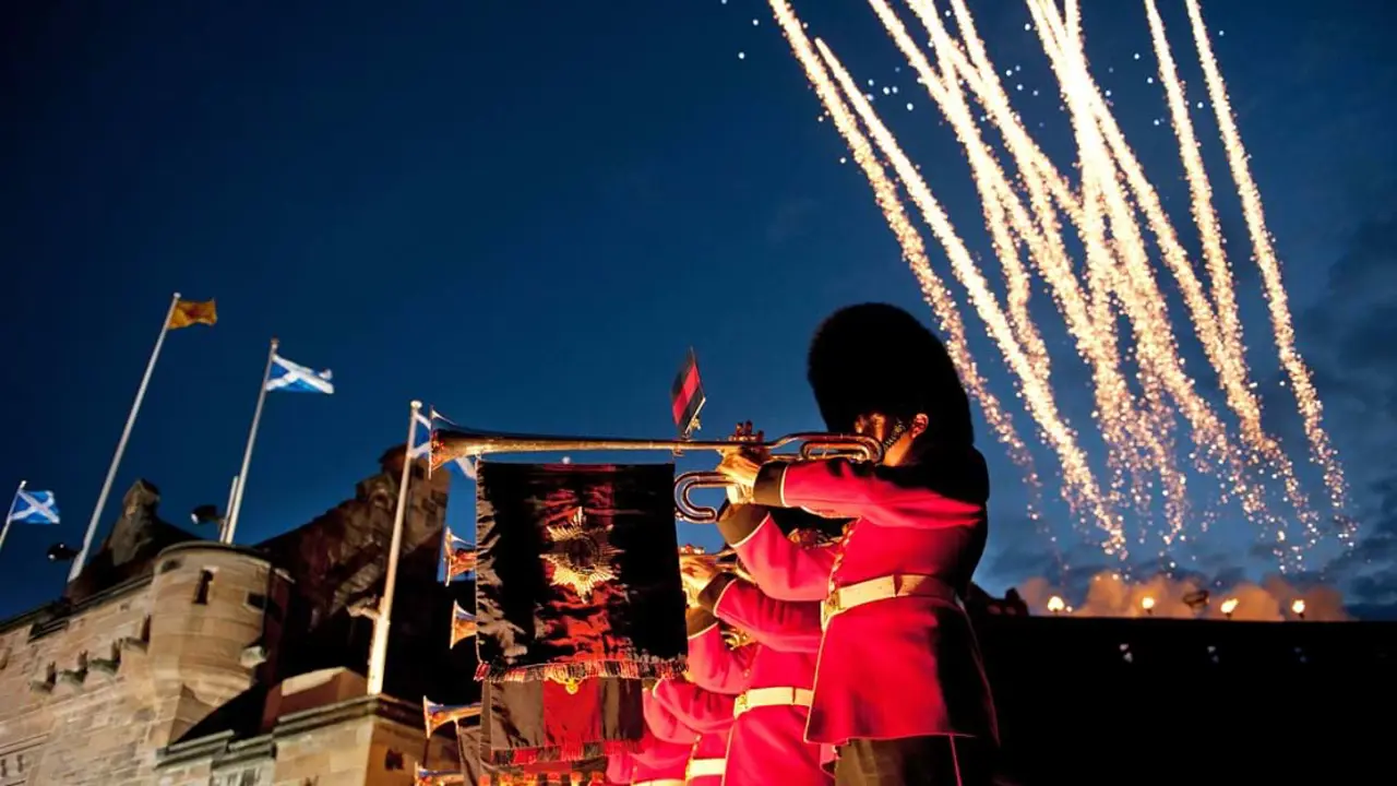 The Royal Edinburgh Military soldiers playing fanfare on trombones, suspended with flags in front of Edinburgh castle and fireworks