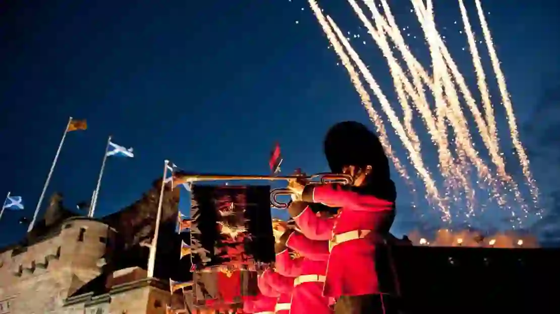 The Royal Edinburgh Military soldiers playing fanfare on trombones, suspended with flags in front of Edinburgh castle and fireworks