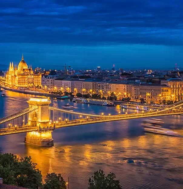 High angle shot of Széchenyi Chain Bridge, going over the Danube River at night time. With a view of the Pest side, the Parliament building in the distance