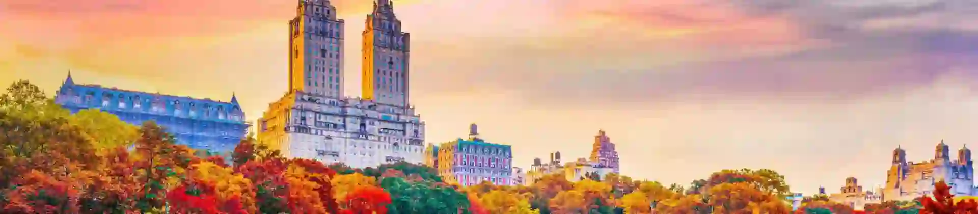 Central Park in autumn with The Lake in the centre, surrounded by colourful trees in shades of red, orange, green and yellow. The iconic twin towers of The San Remo rise in the background