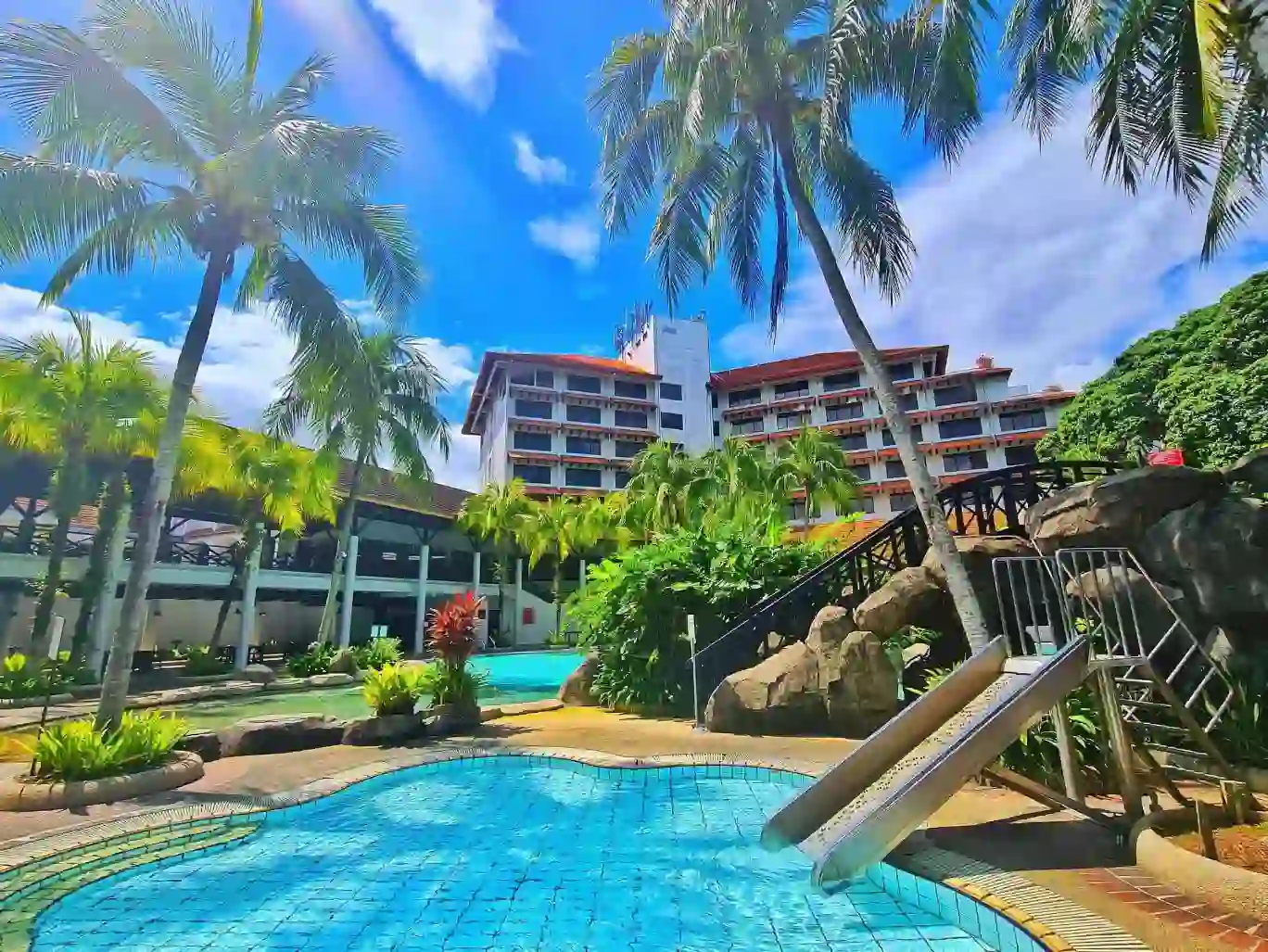 Two outdoor swimming pools at Sabah Hotel, Sandakan, with the hotel building in the background, surrounded by palm trees