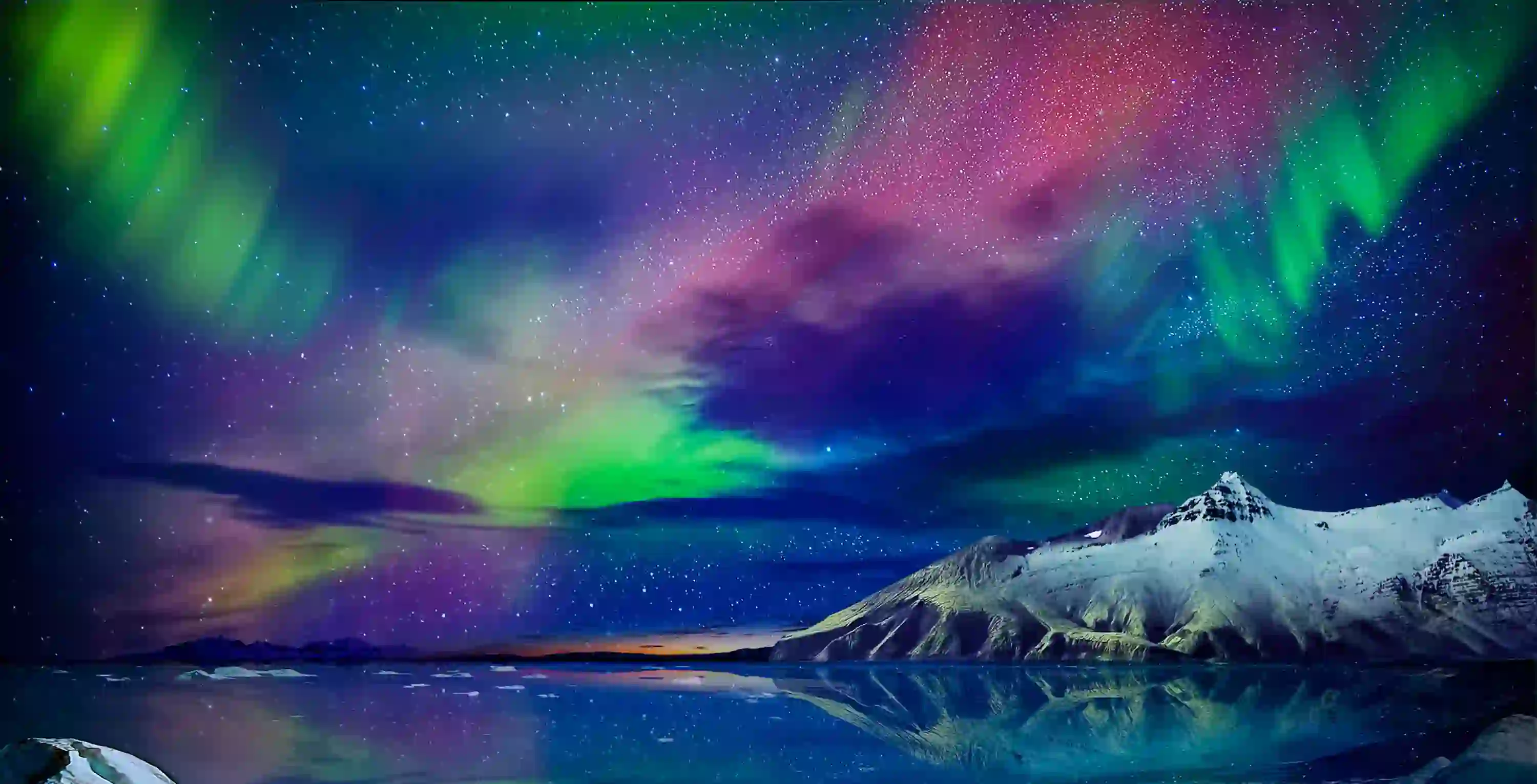 Starry sky with green, purple and blue Northern Lights. Below, a lake and a snowy mountain