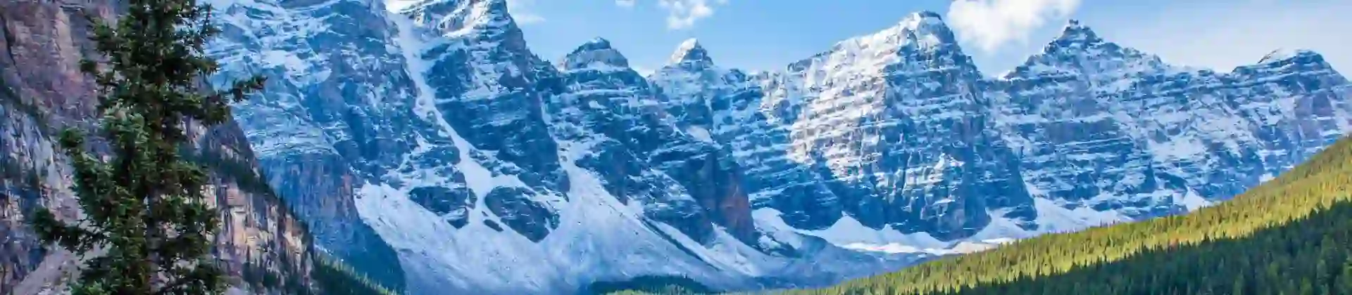Snow-capped Rocky Mountains towering over the serene, turquoise Moraine Lake in Canada, with dense pine forests lining the shores and a clear blue sky above