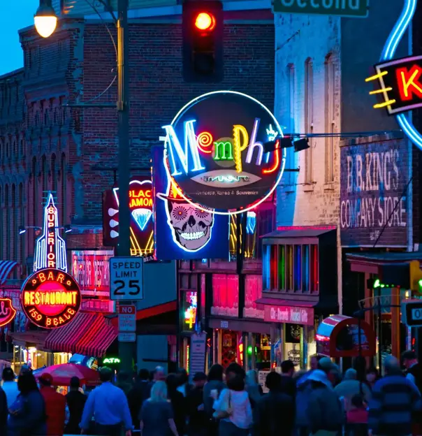 Vibrant night scene of Beale Street in Memphis, Tennessee, with colourful neon signs for bars, restaurants, and blues clubs, and a crowd of people walking along the street