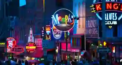 Vibrant night scene of Beale Street in Memphis, Tennessee, with colourful neon signs for bars, restaurants, and blues clubs, and a crowd of people walking along the street