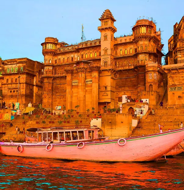 The ghats of Varanasi seen from the River Ganges, with historic sandstone palaces and colourful boats reflecting in the calm evening water