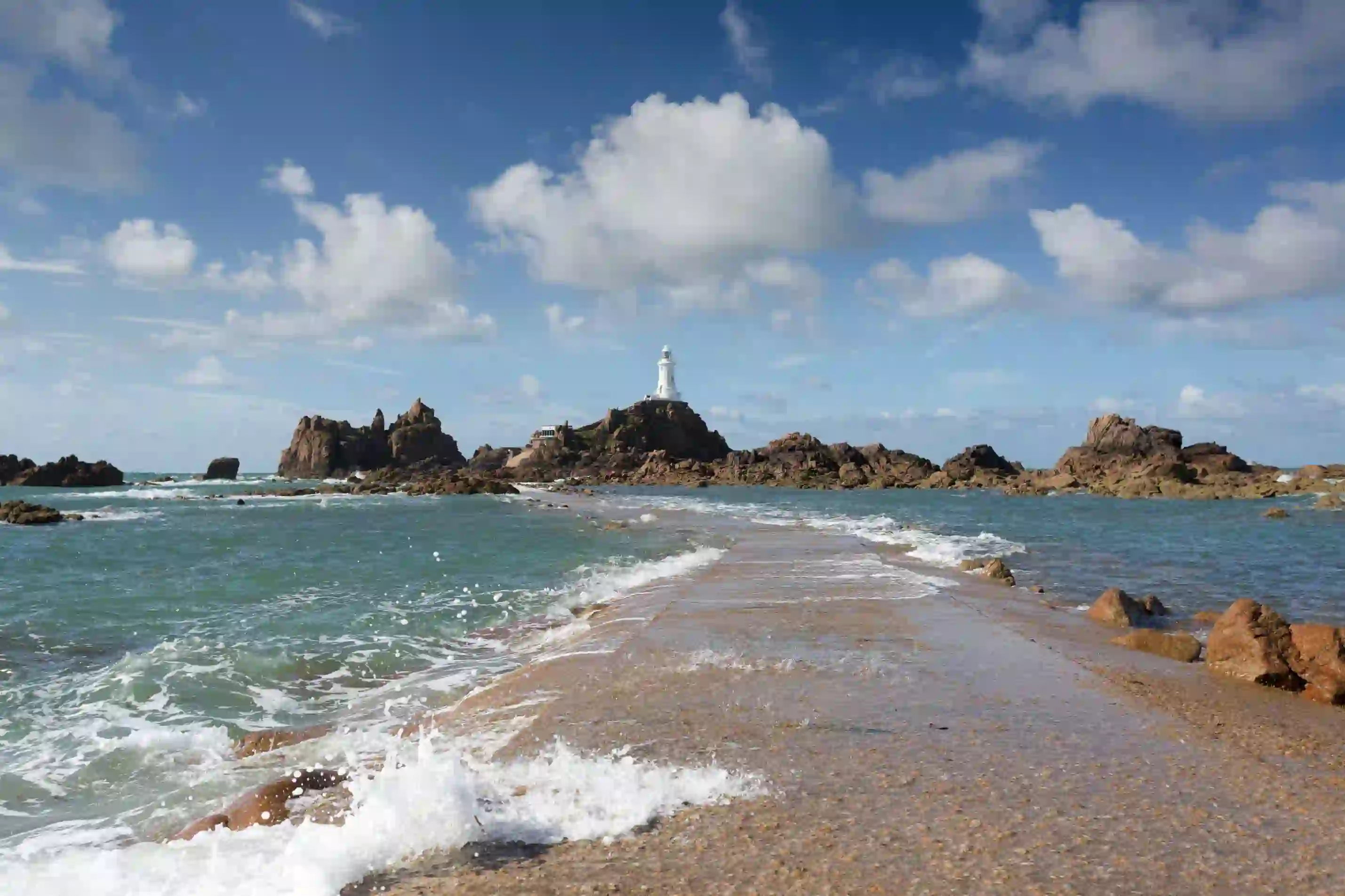 Long shot of the La Corbiere Causeway Light house, showing the sea below it, the rocks either side of it and a stone panel which runs towards it across the water