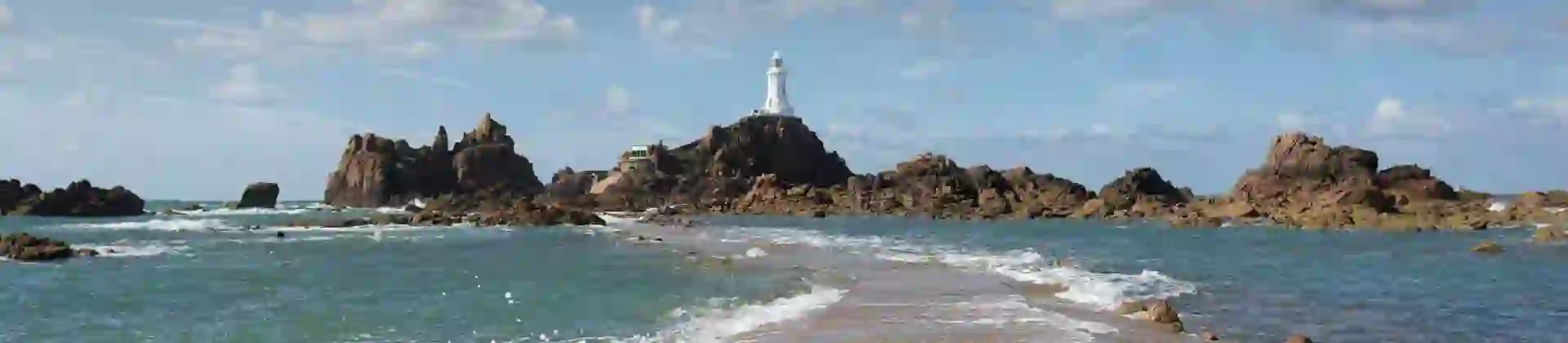 Long shot of the La Corbiere Causeway Light house, showing the sea below it, the rocks either side of it and a stone panel which runs towards it across the water