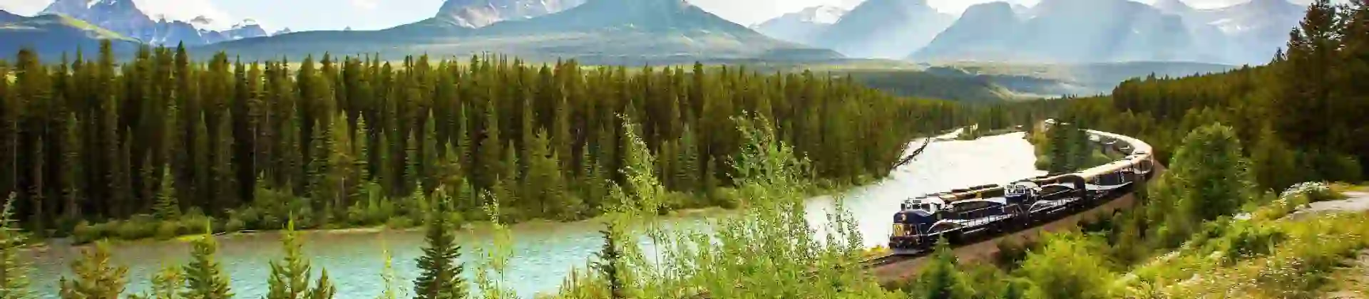 The Rocky Mountaineer train travelling through the Canadian Rockies, with rugged mountains in the background and dense evergreen forests lining the tracks